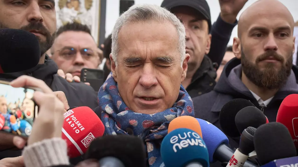 Călin Georgescu, candidatul de extremă dreapta, în timpul unu interviu, cu microfoane lângă el, cu un fular de culoare albastră la gât, și cu ochii închiși