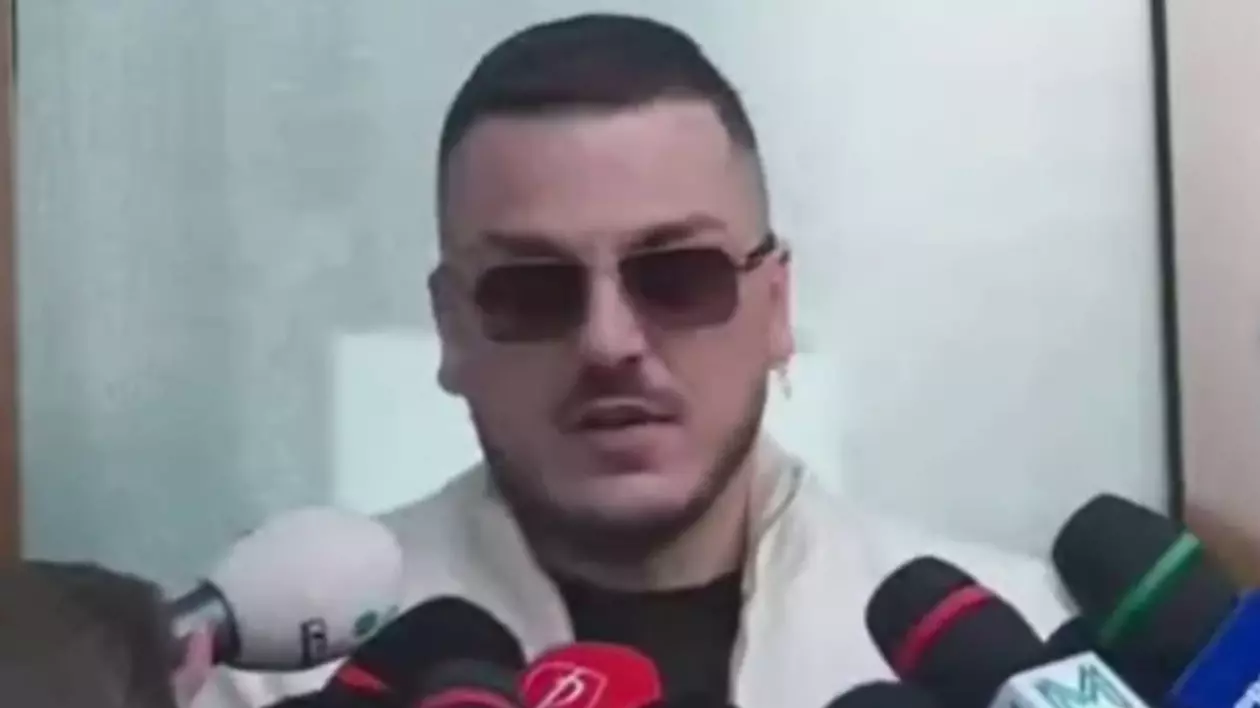 Makaveli, influencerul de pe TikTok, purtând o pereche de ochelari de soare, în fața sediului Poliției, în București, în timp ce poartă o geacă de culoare albă