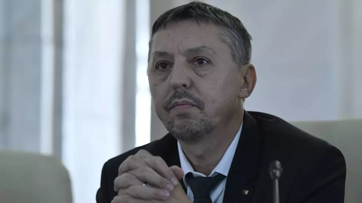 ministrul educatiei Daniel David purtand un sacou negru si camasa alba, aflat la un birou, tinand mainile imperecheate
