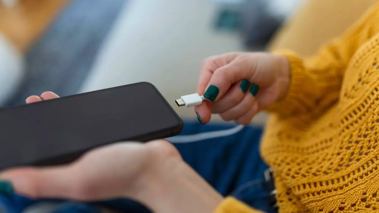 mainile unei femei care conecteaza cablul de incarcare in telefonul mobil