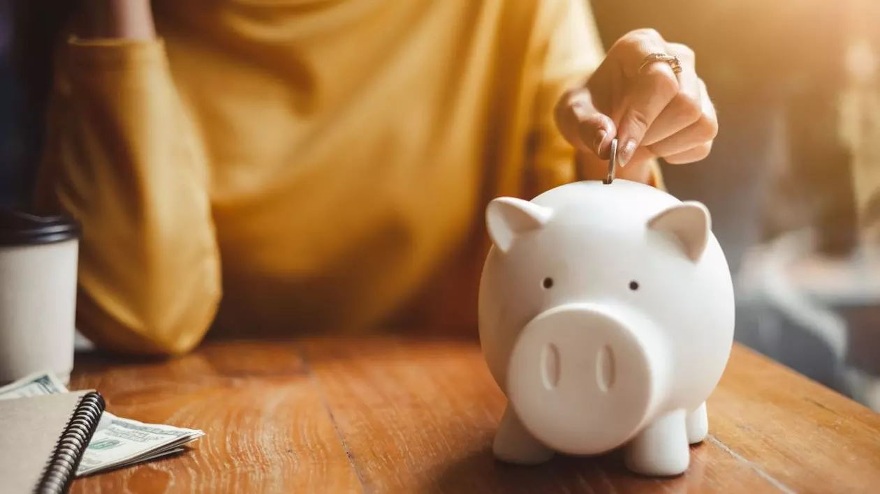 O femeie pune bani într-o pușculiță de tip porc alb, aflată pe o masă. Foto cu caracter ilustrativ: Shutterstock