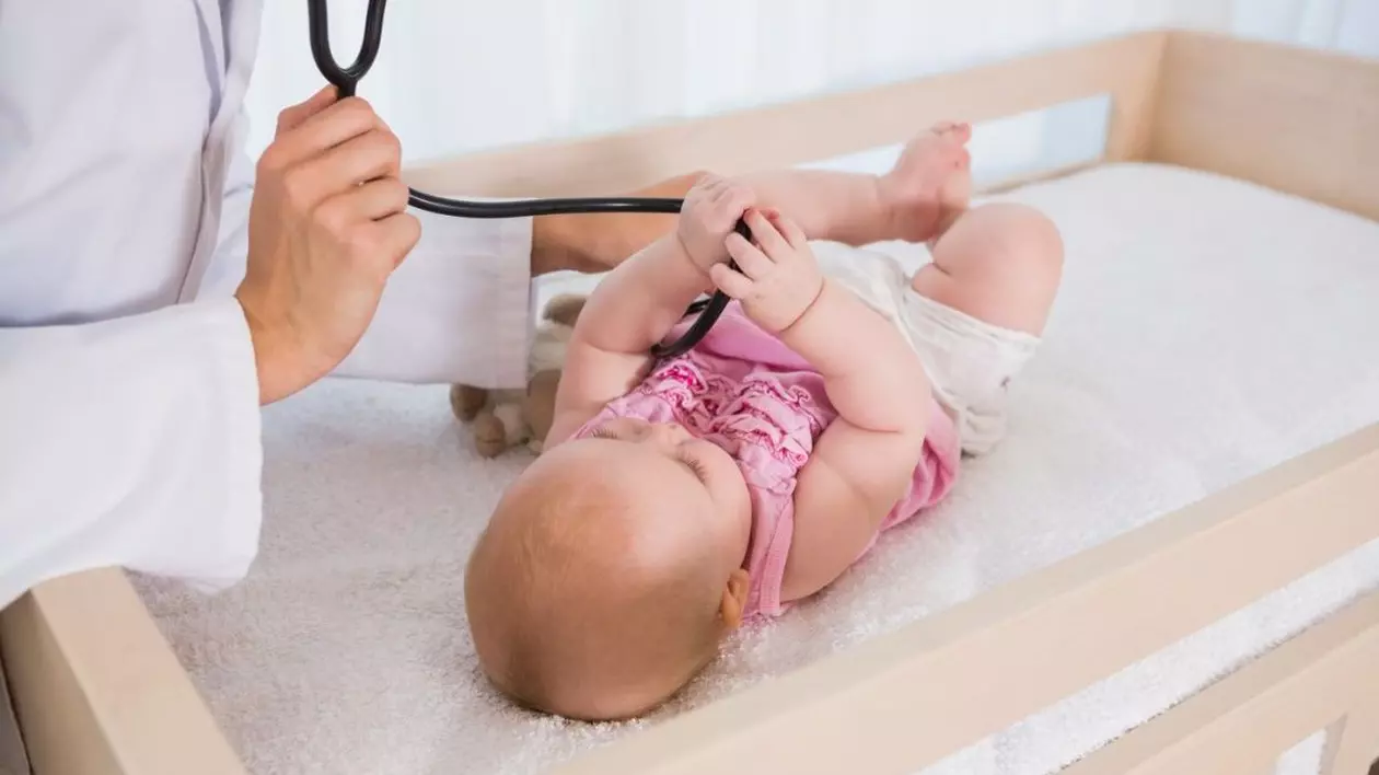 O fetiță care stă pe un pat de spital se joacă cu stetoscopul medicului care o consultă