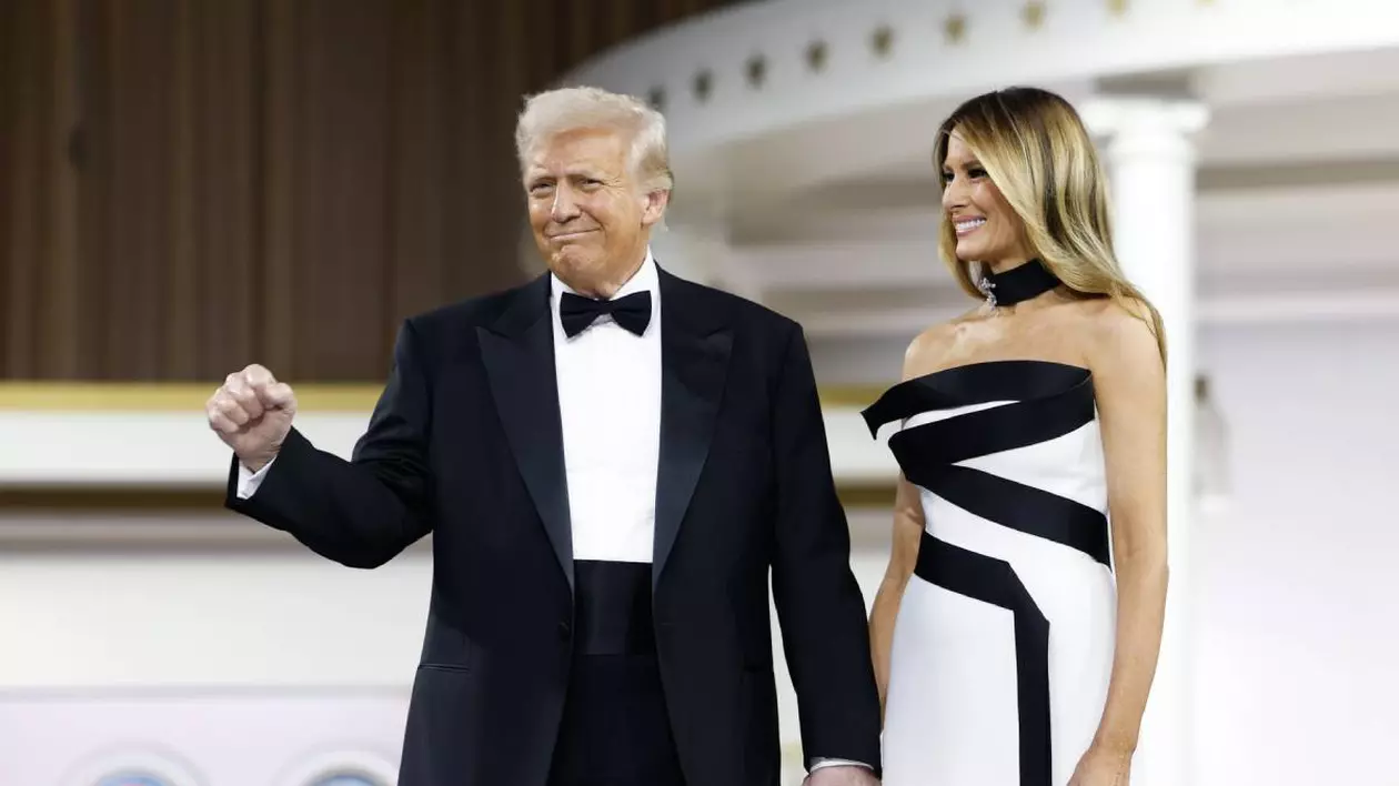 donald trump purtand un costum negru cu camasa alba tinand mana ridicata cu pumnul strans alaturi de melania trump care poarta o rochie alba cu un model nergu