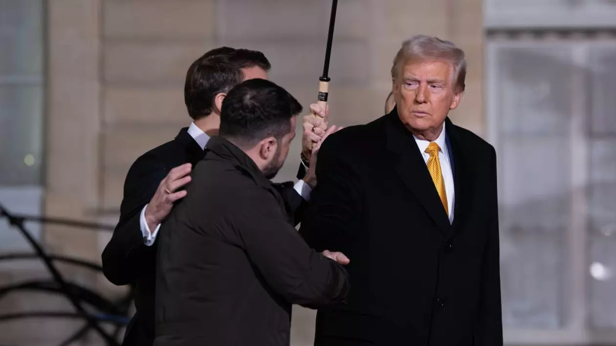 donald trump imbracat cu o camasa alba si palton negru in timp ce da mana cu volodimir zelenski. in spatele lor este emanuel macron