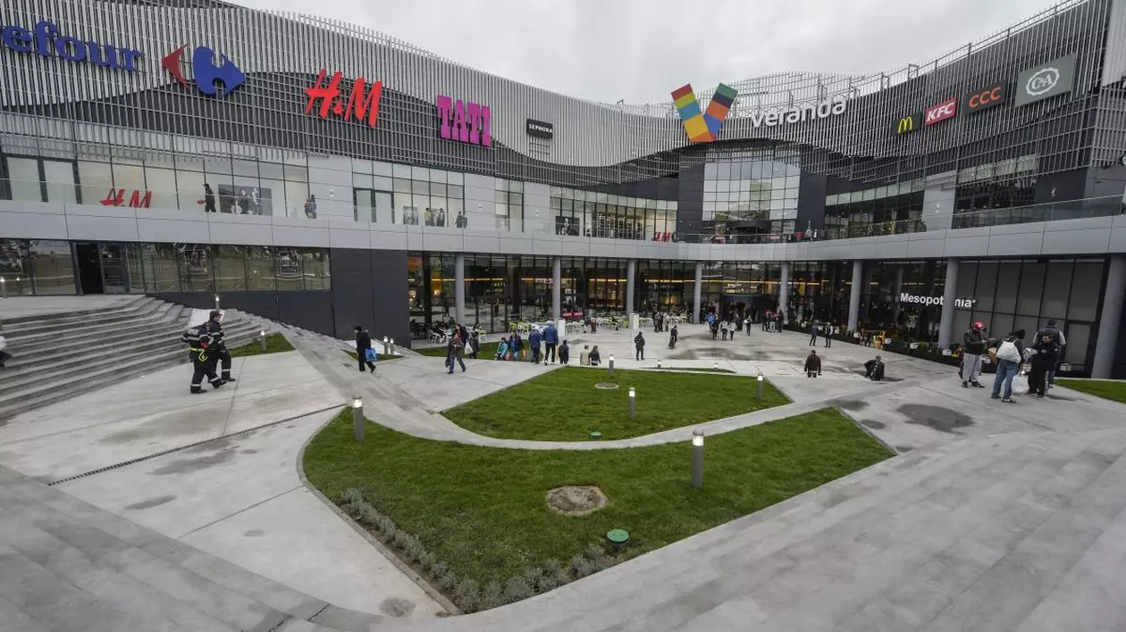 Mai multe persoane sunt în fața mall-ului Veranda din București și intră în centrul comercial, iar în prim-plan este amenajat un spațiu verde