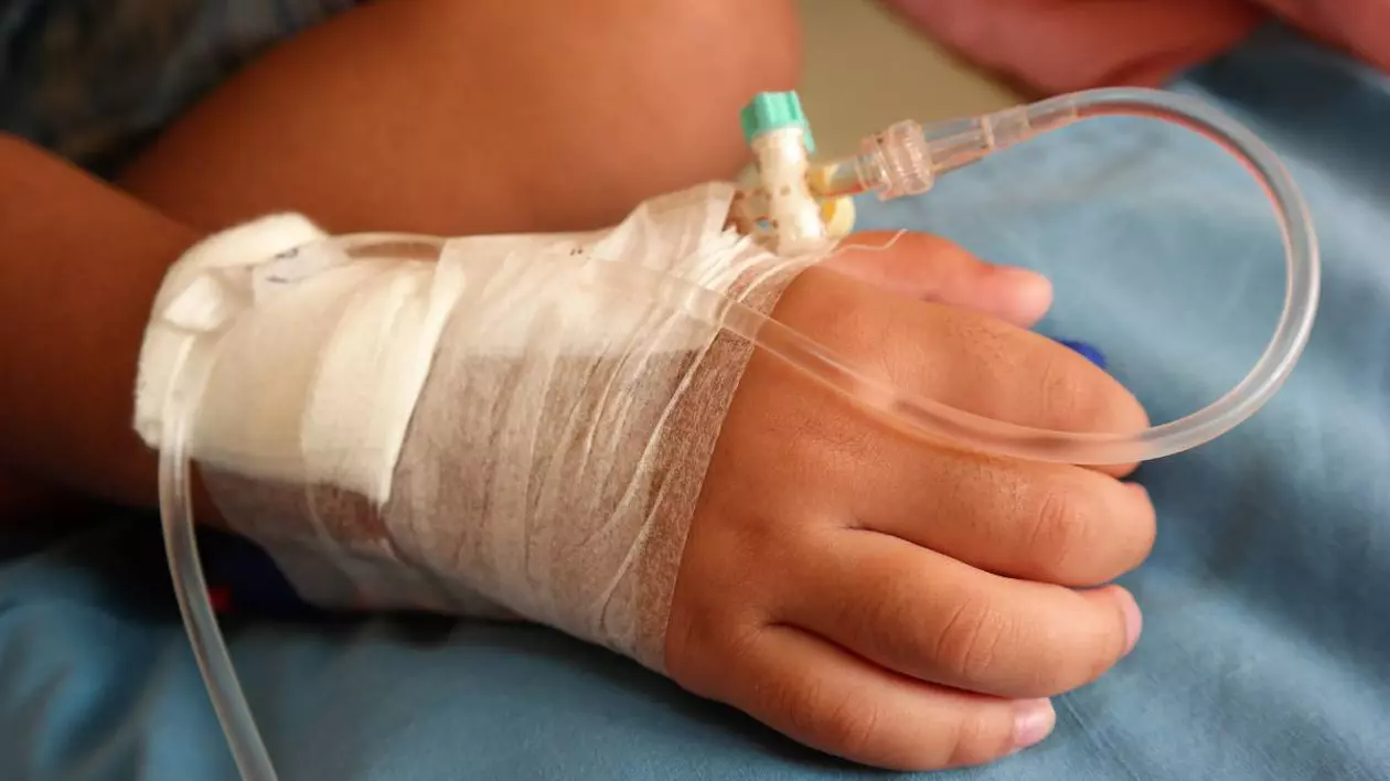 Copil cu o branulă în mână, pe un pat de spital
