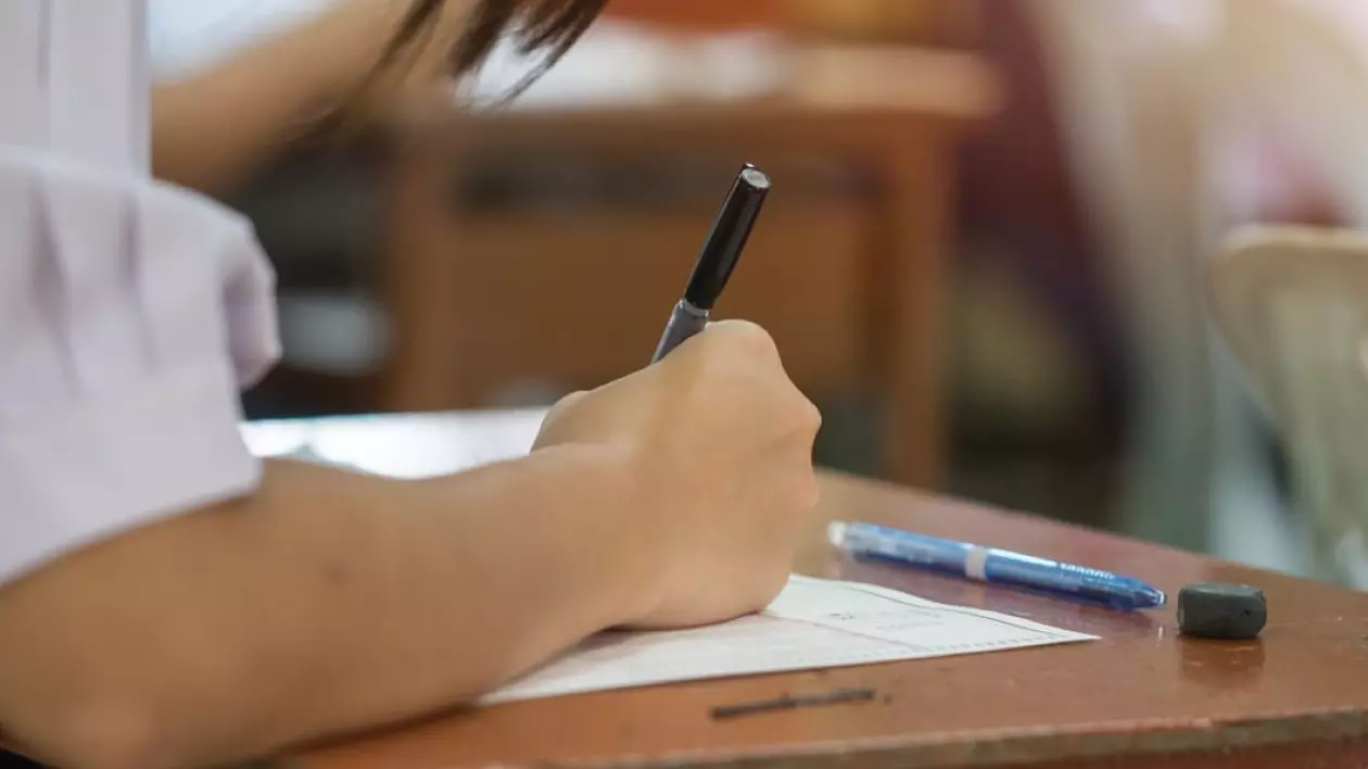Mâna unui elev care scrie pe hârtia pusă pe bancă, la Evaluarea Națională 2025