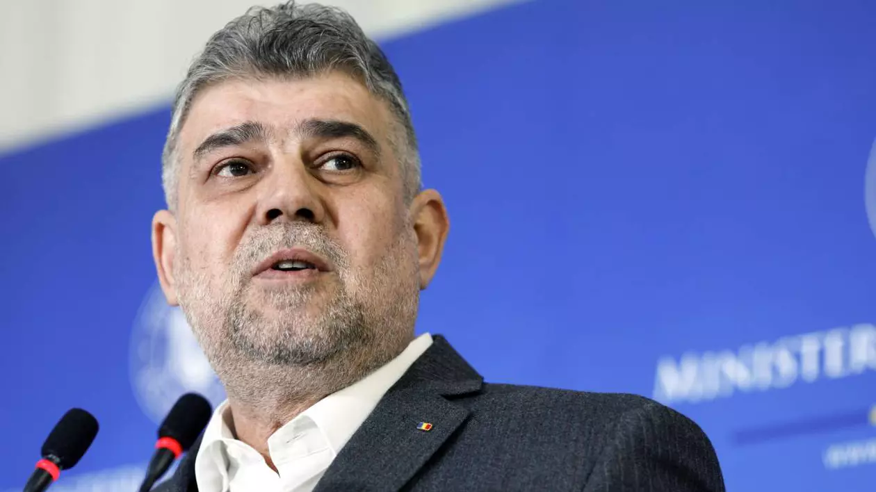 premierul marcel ciolacu vorbind la microfon in timpul unei conferinte imbracat cu camasa alba si sacou gri