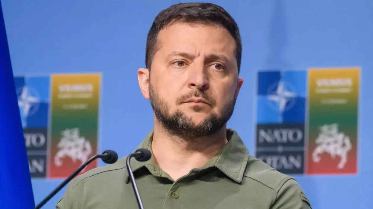 volodimir zelenski in fata unui microfon tinand un discurs, in spate are un wall cu sigla nato