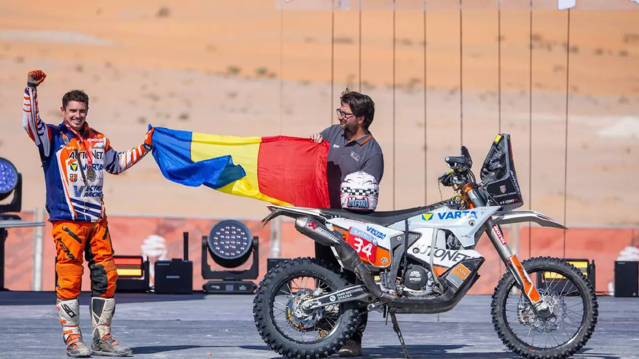 raider roman castigat dakar 2025 tine in mana drapelul romaniei, langa el este motocicleta sa