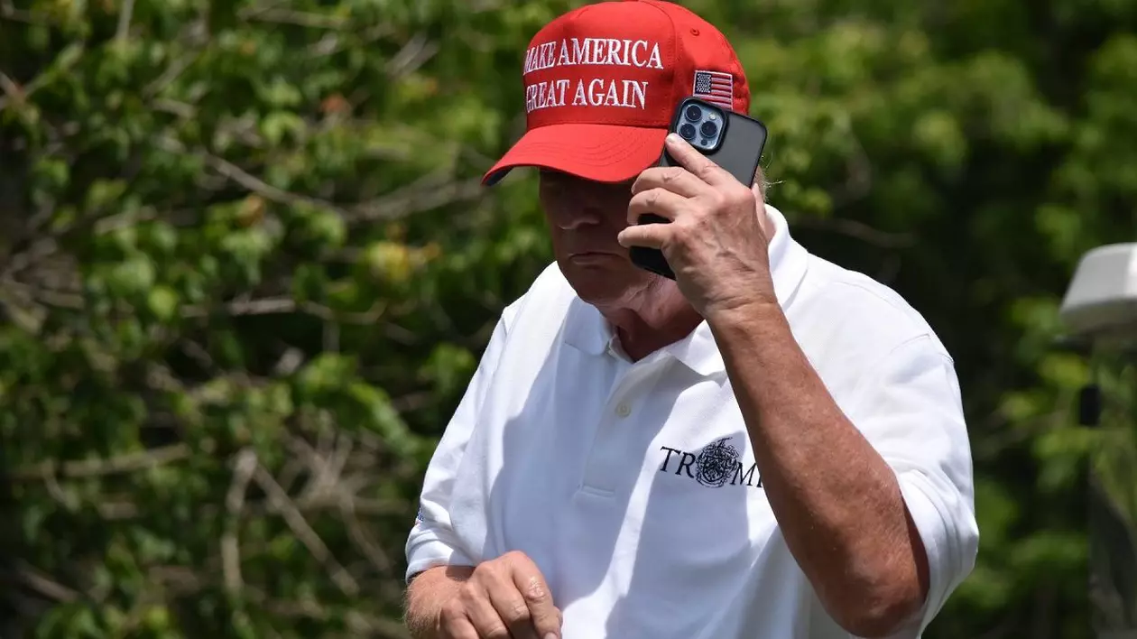 Donald Trump, în tricou alb și cu șapcă neagră, vorbește la telefon