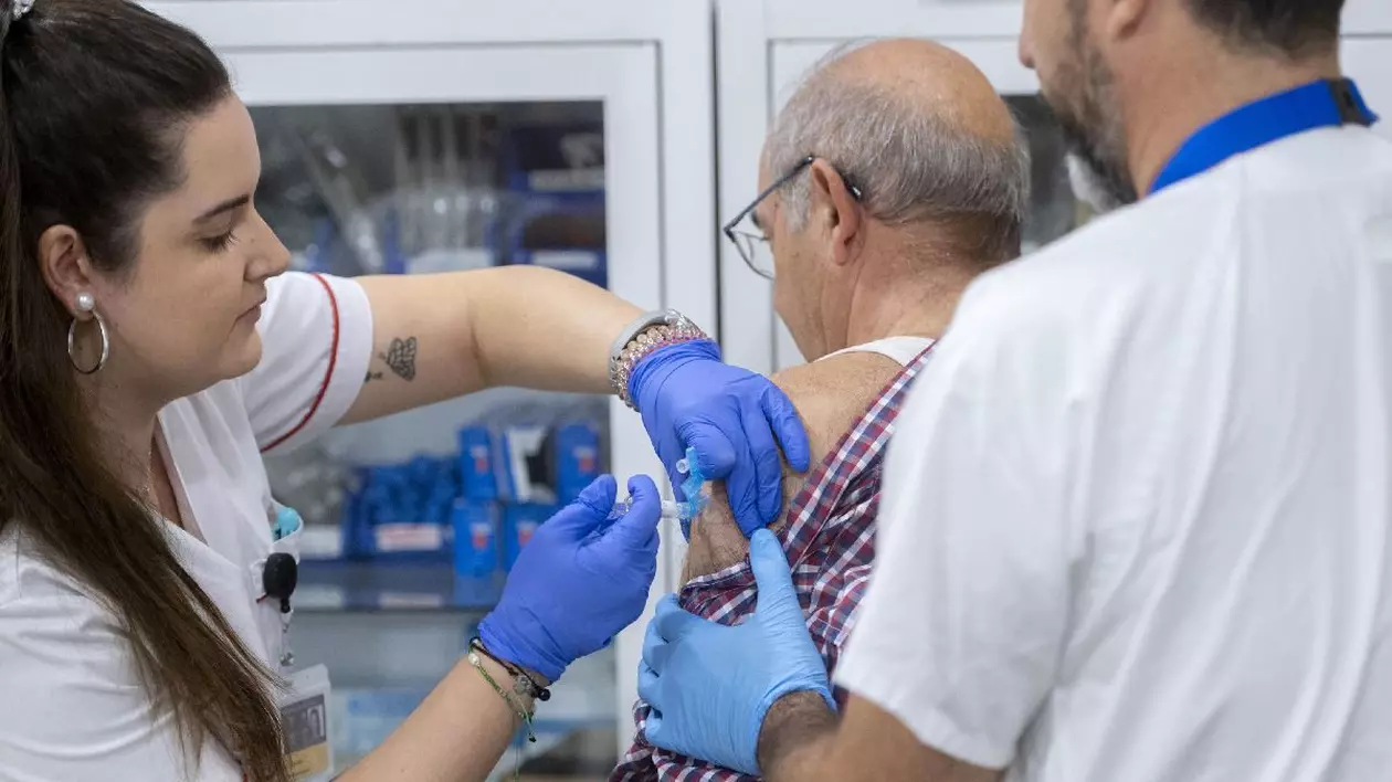 O asistentă vaccinează antigripal un bătrân, într-un spital