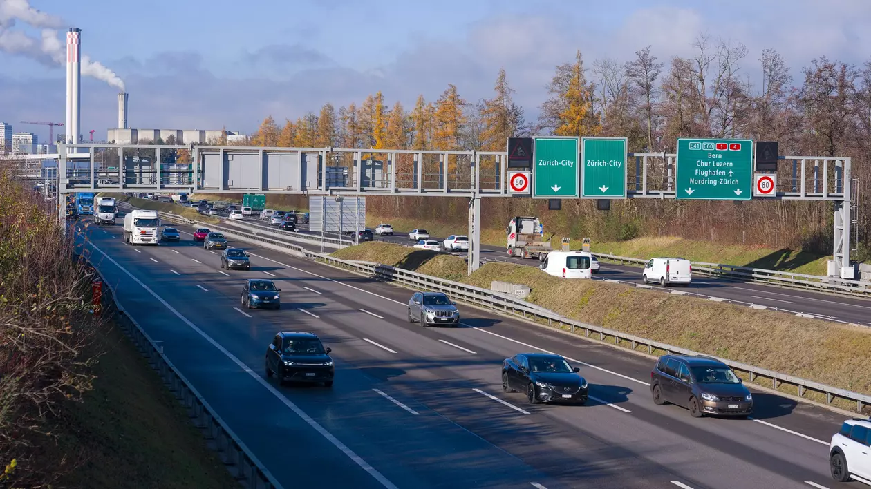autostradă din Elveția, în apropierea orașului Zurich pe care circula mai multe masini si camioane. in dreapta se observa indicatoare rutiere care indica directia pentru orasul zurich
