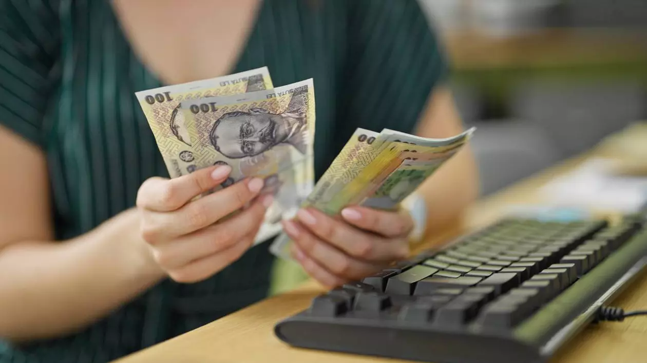 femeie care numara mai multe bancnote romanesti in fata ei are o tastatura de calculator