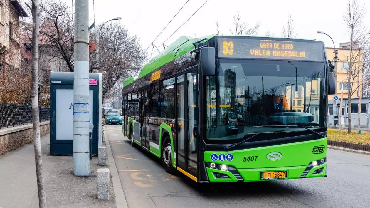 Un troleibuz verde al liniei 93 este în stație, iar lângă aceasta se văd câteva case și copaci cu frunze uscate