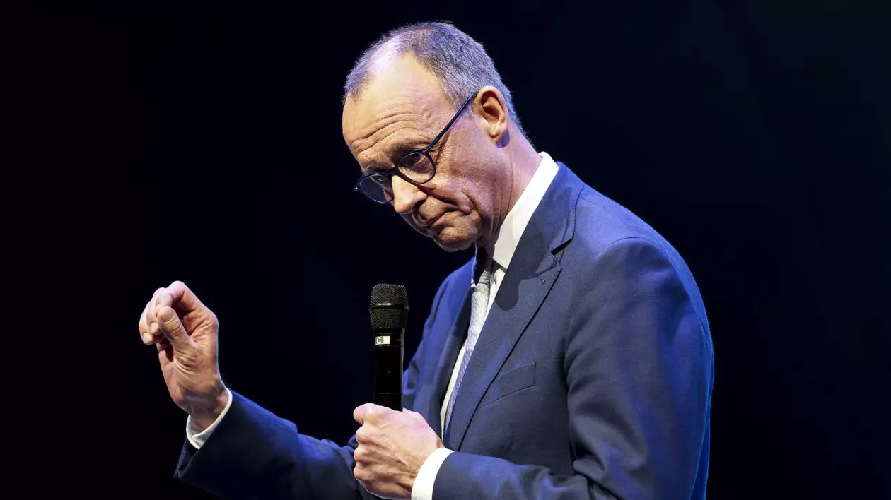 Friedrich Merz vorbește la microfon și este cu capul în jos, având un fundal negru în spate