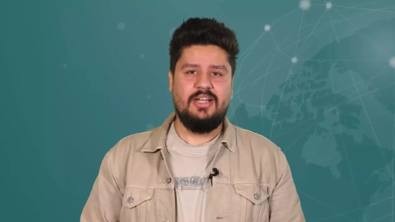 Claudiu Răpan, gazda rubricii 5 știri by Libertatea - Tech, în studiul emisiunii, îmbrăcat cu un tricou de culoare crem și un sacou de aceeași culoare