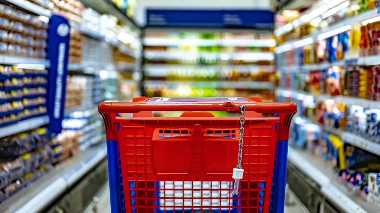 Un coș de cumpărături roșu se vede pe culoarul unui supermarket