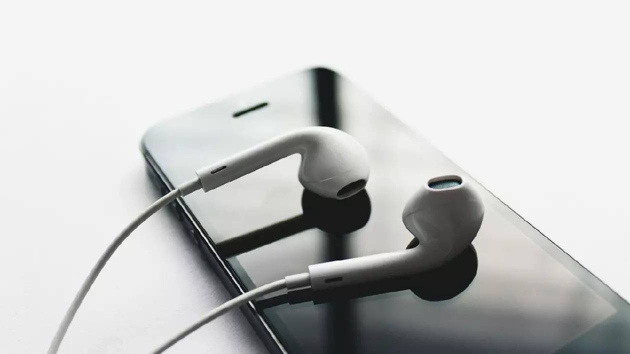 O pereche de căști Apple albe cu fir, așezate pe ecranul unui iPhone.