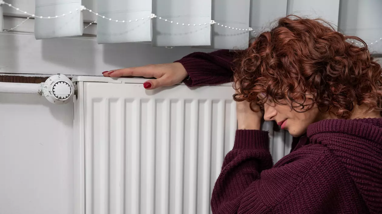 De ce nu se mai încălzește caloriferul – cauze și soluții - Imagine cu o femeie ghemuită lângă un calirifer