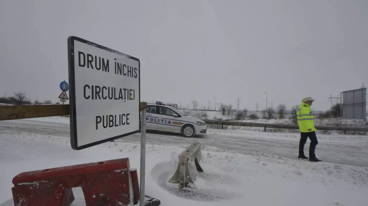 indicator rutier drum inchis circlatie, o masina de politie pe fundal, iar langa un politist. drumul este acoperit cu zapada