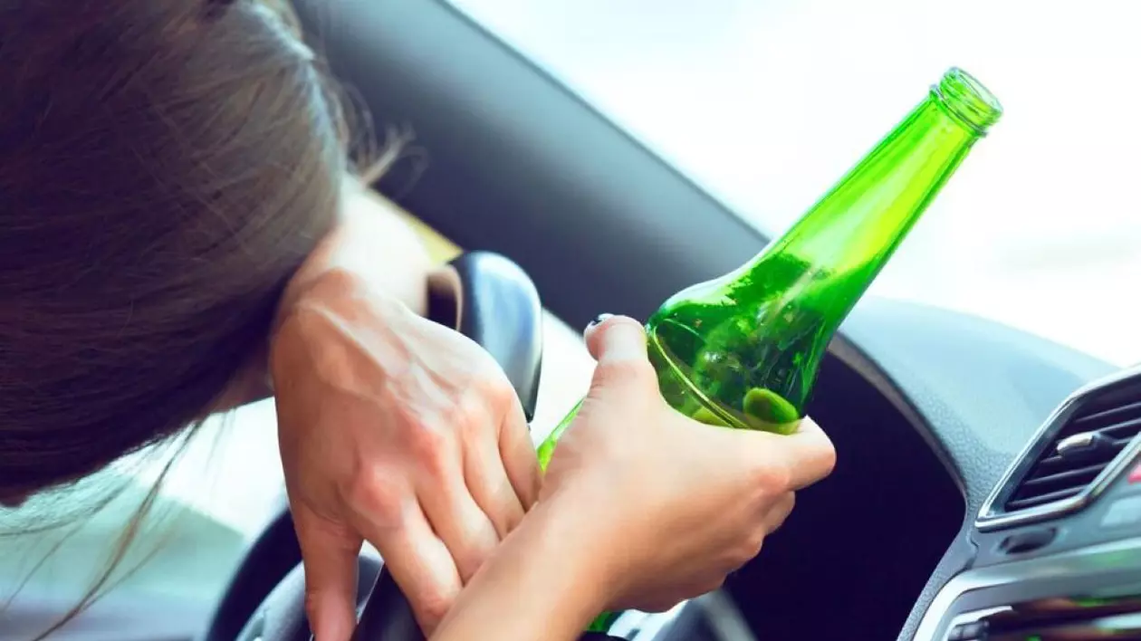 Femeie băută la volan. Stă cu capul pe volan, iar în mâna dreaptă are o sticlă cu alcool
