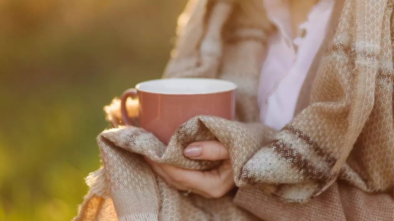 femeie în pătură cu model cu dungi care ține în mână o cană de ceai roz