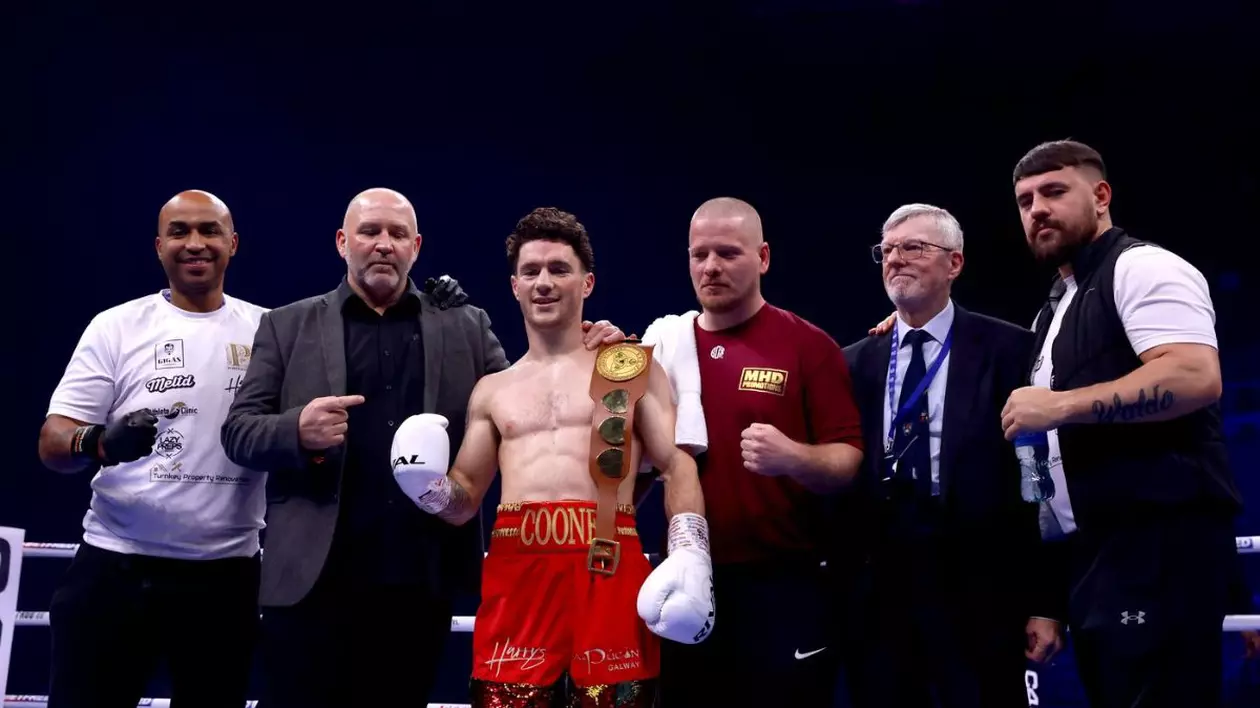 Fotografie de arhivă datată 251123 a boxerului irlandez John Cooney (centru), îmbrăcat într-o pereche de pantaloni scurți roșii cu o banderola pe care este scris numele său, alături de staff și antrenori