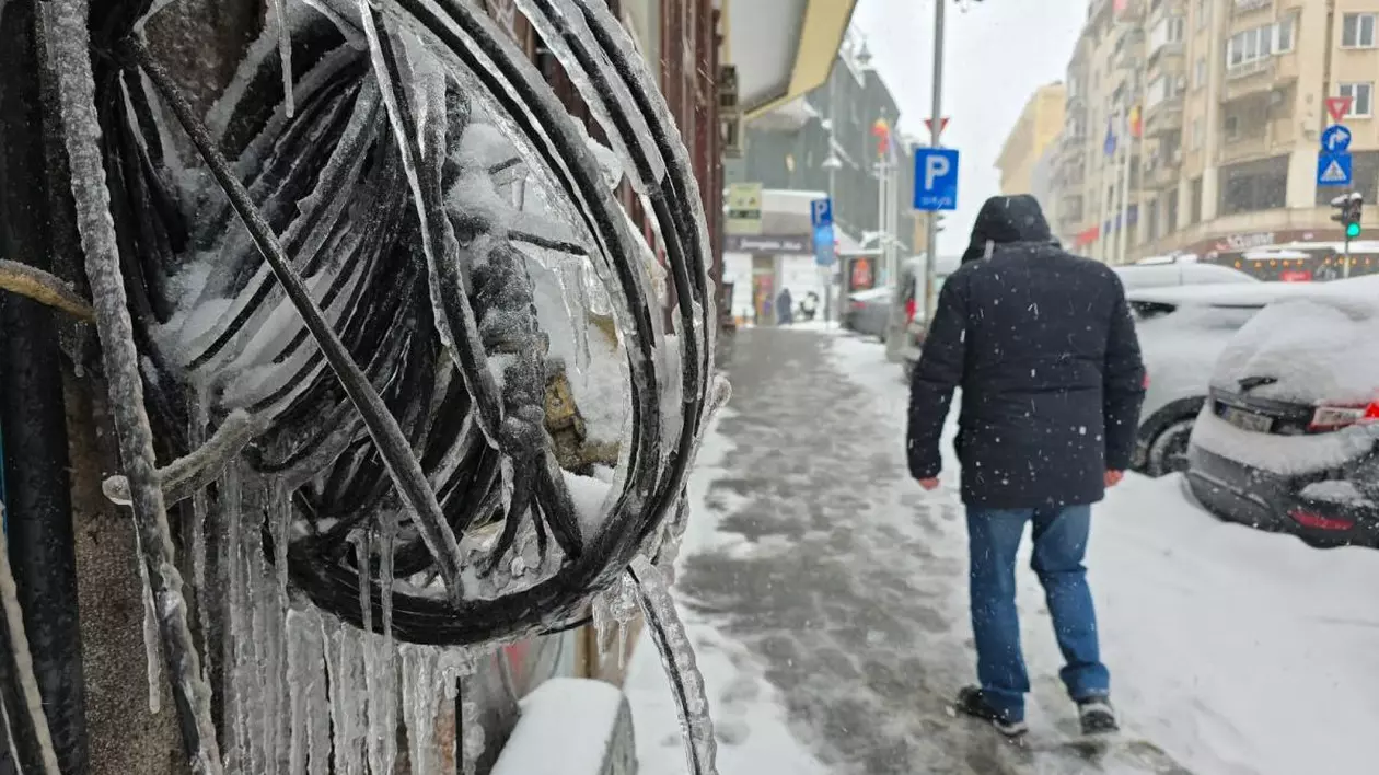 O zi geroasă în România, în care cablurile de pe peretele unei case au înghețat și se văd țurțurii, iar un bărbat merge pe jos, unde este zăpadă și gheață