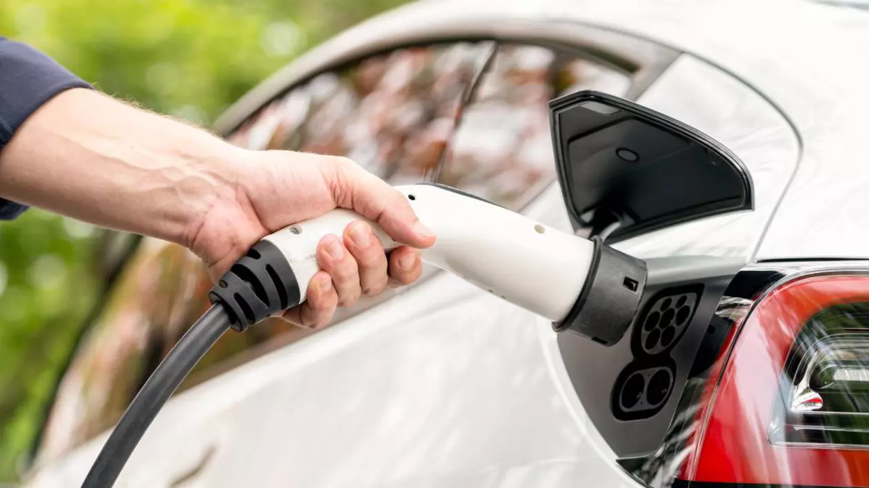 persoana care tine in mana incarcator auto langa o masina alba electrica