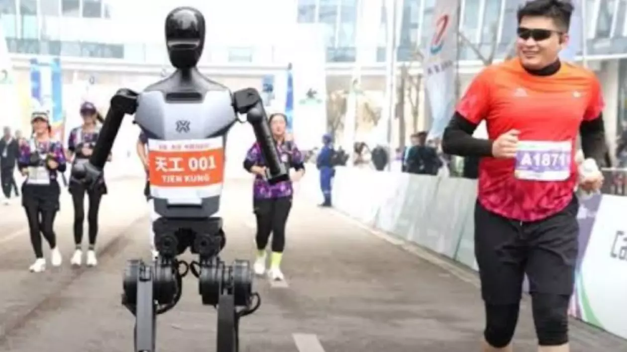 Un robot umanoid și un om trec linia de sosire la o competiție sportivă. Tânărul se uită cu admirație către oponentul său