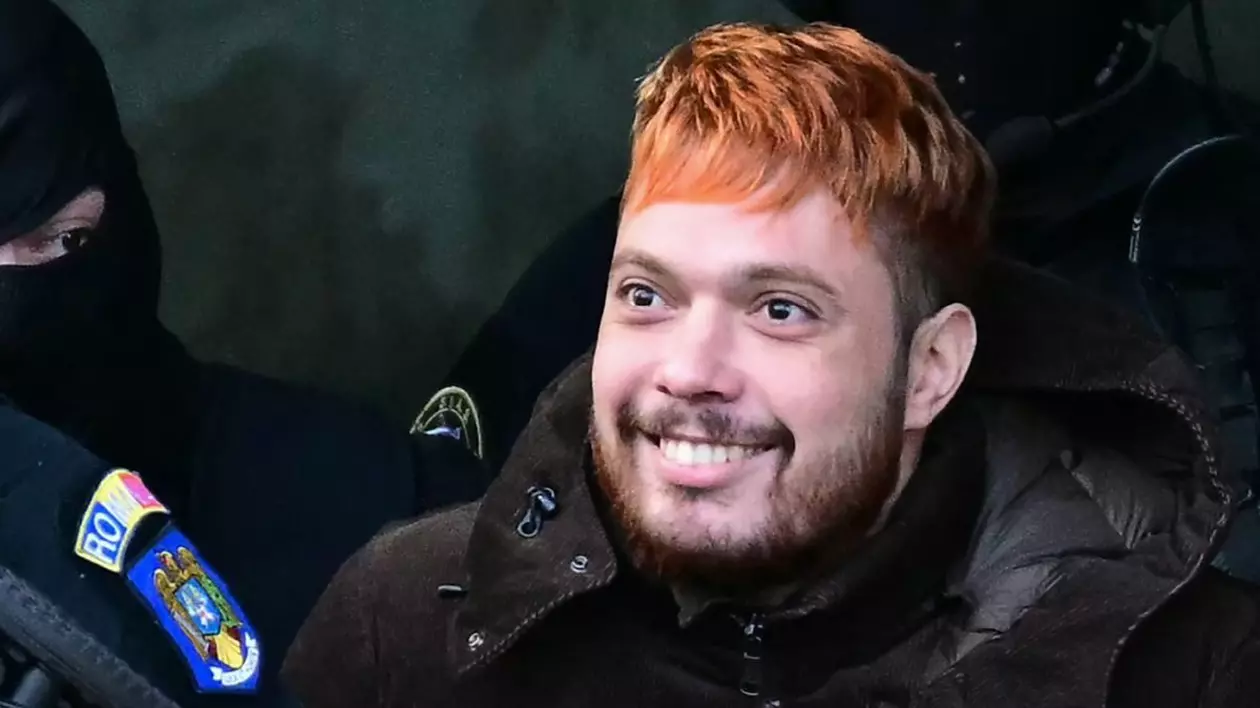 Mohamed Amra, criminalul francez prins la București, în imagine cu părul roșu și geacă neagră, ținut de un polițist mascat