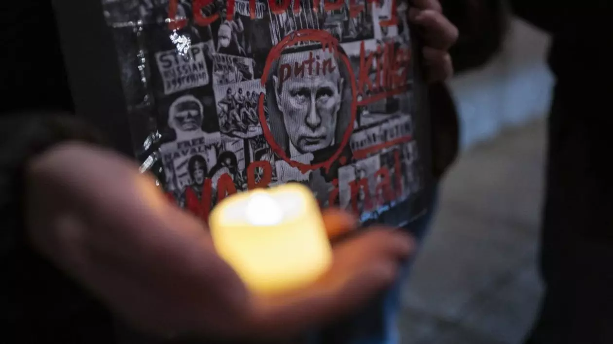 Un bărbat ține în mână un afiș cu fața lui Putin și în altă mână o lumânare aprinsă, în memoria victimelor războiului din Ucraina Foto: Profimedia
