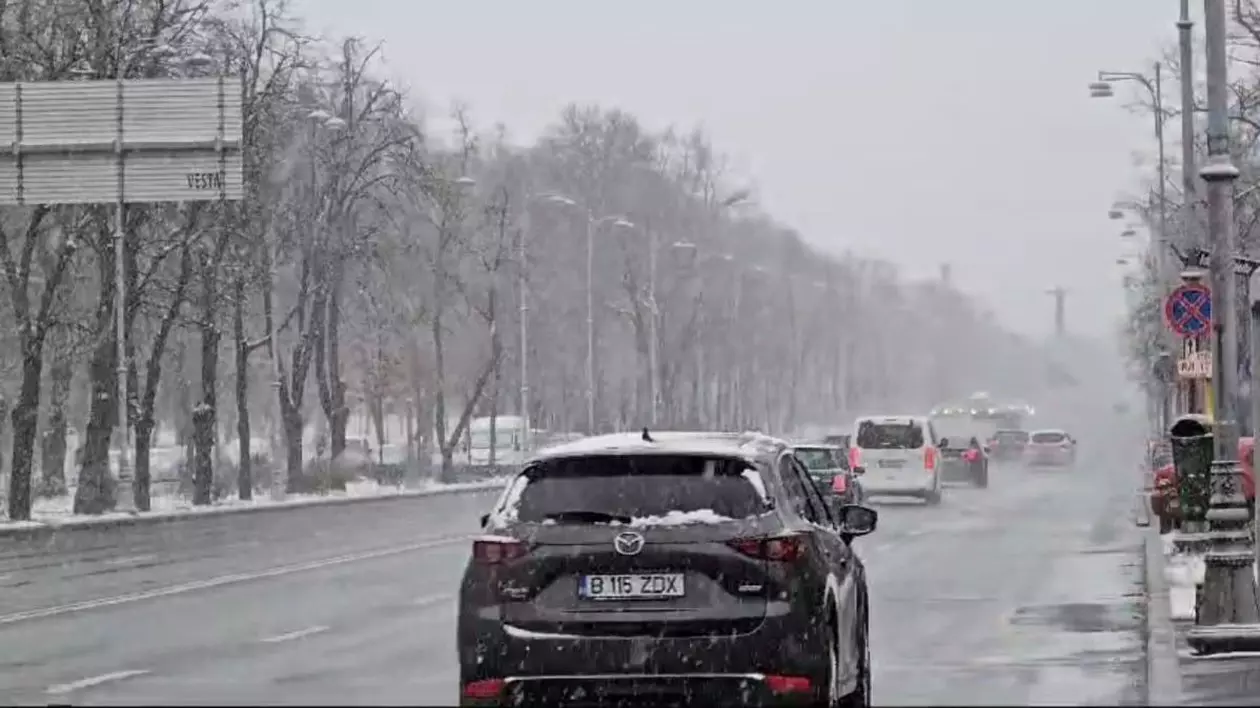 Mai multe mașini circulă pe Bulevardul Aviatorilor din București, pe timp de iarnă, iar pe străzi se vede ninsoare