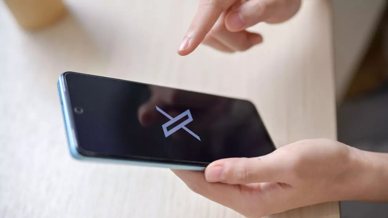 O imagine în prim plan a unei mâini de femeie care ține un smartphone cu logo-ul X pe ecran la o masă în interior. social media