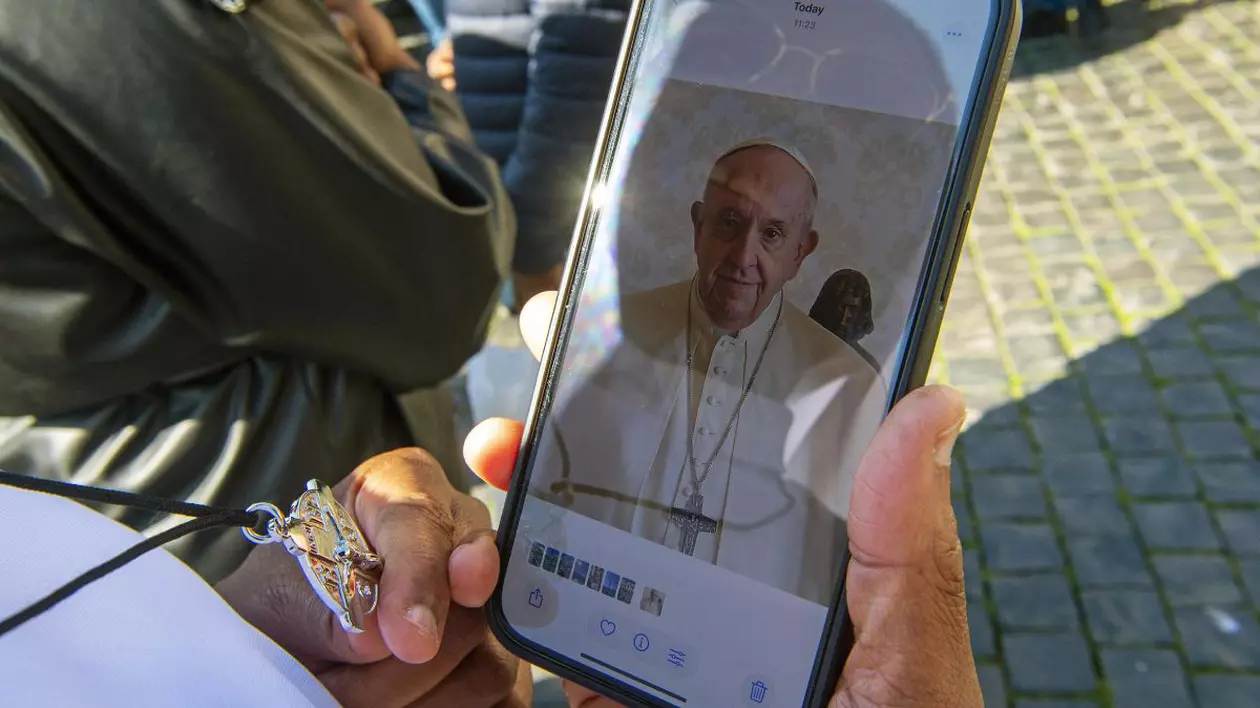 Persoană necunoscută ține în mână un telefon mobil cu o fotografie a Papei Francisc în Piața Sfântul Petru din Vatican