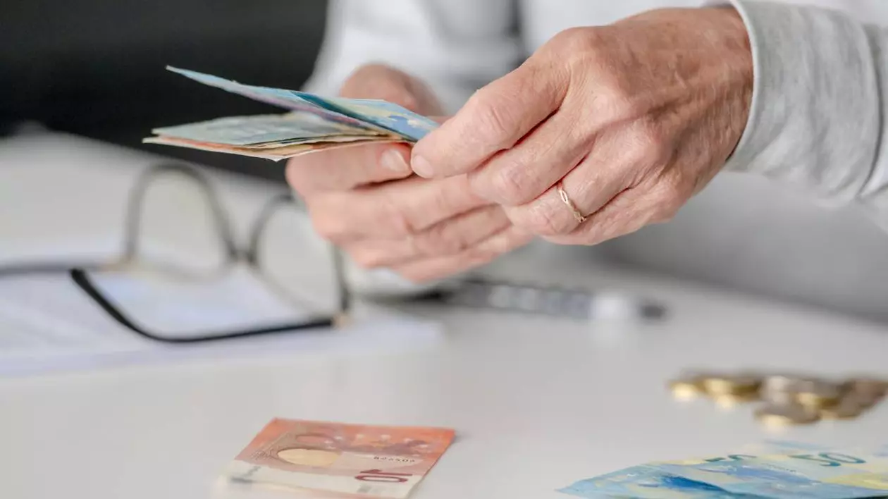 mainile unui batran care numara cateva bancnote in euro