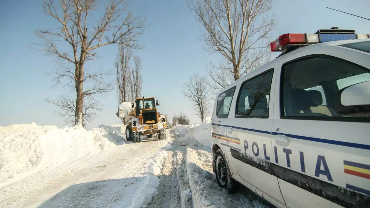masina politiei romane pe un drum inzapezit, in spate se observa un utilaj de deszapezire