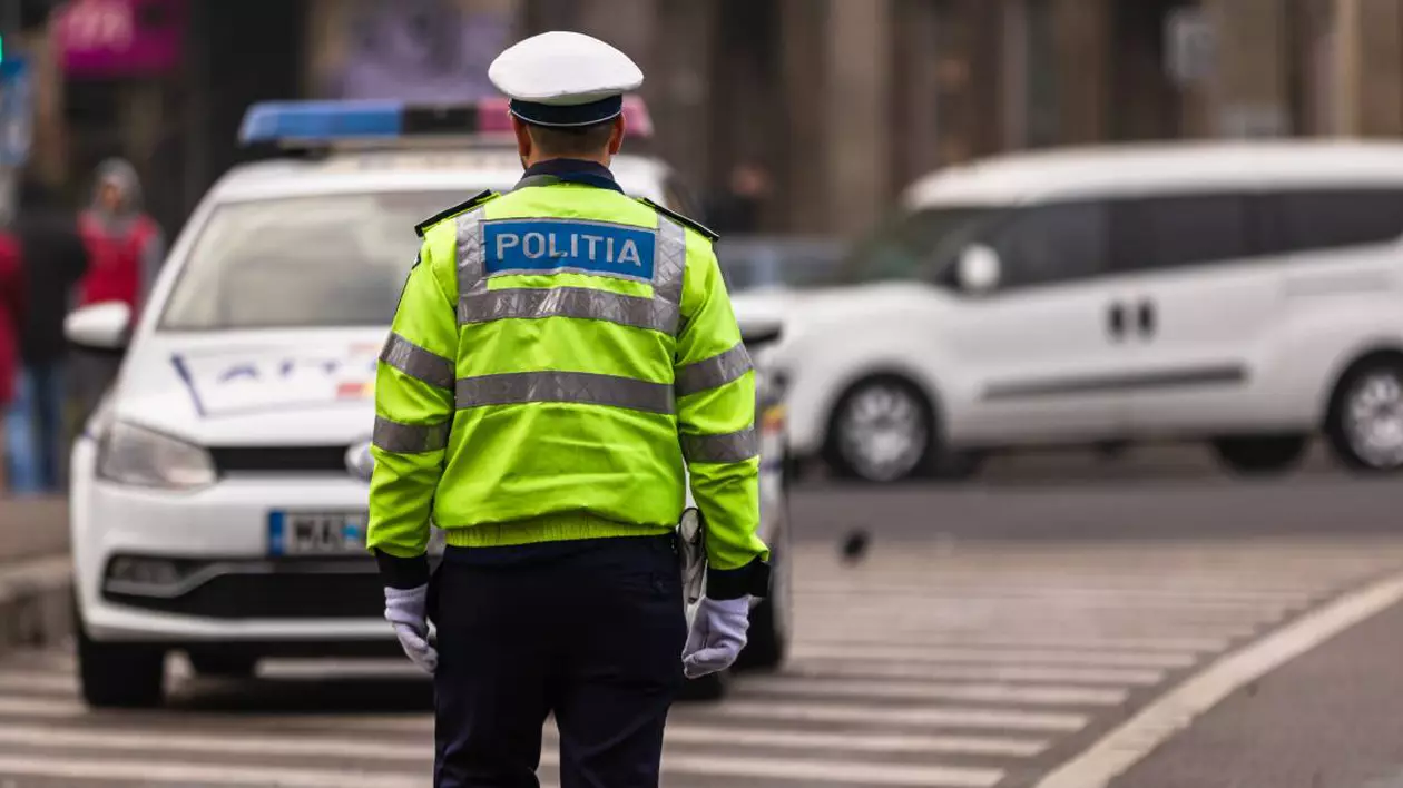 politist imbracat in uniforma in fata lui este autospeciala de politie
