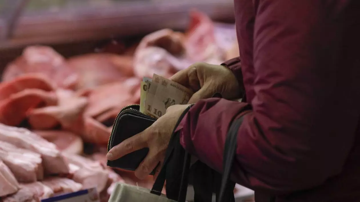 o femeie care cauta bani in portofel, se observa canteva bancnote. pe fundal o vitrina in care este expusa carne