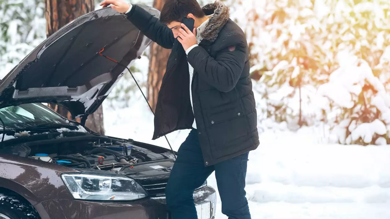 barbat care sta langa masina cu capota deschisa vorbind la telefon, se observa ca este intr-o zona in care a nins foarte mult