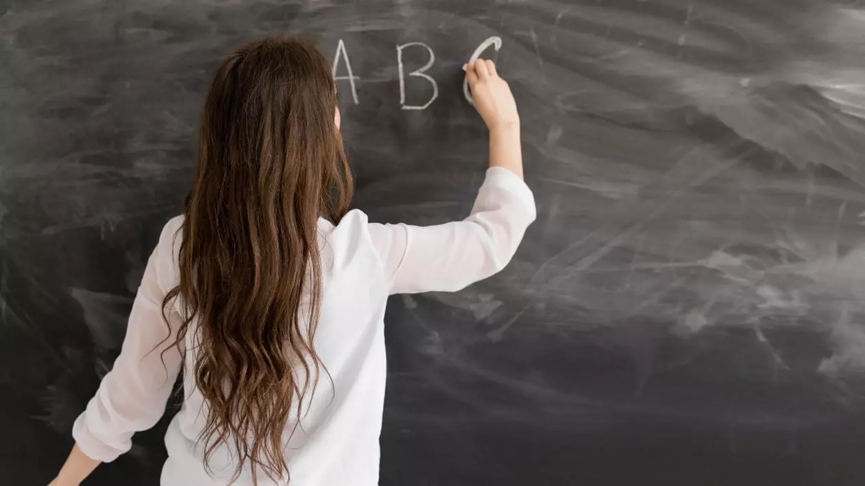 profesoară care scrie litere pe o tablă cu cretă