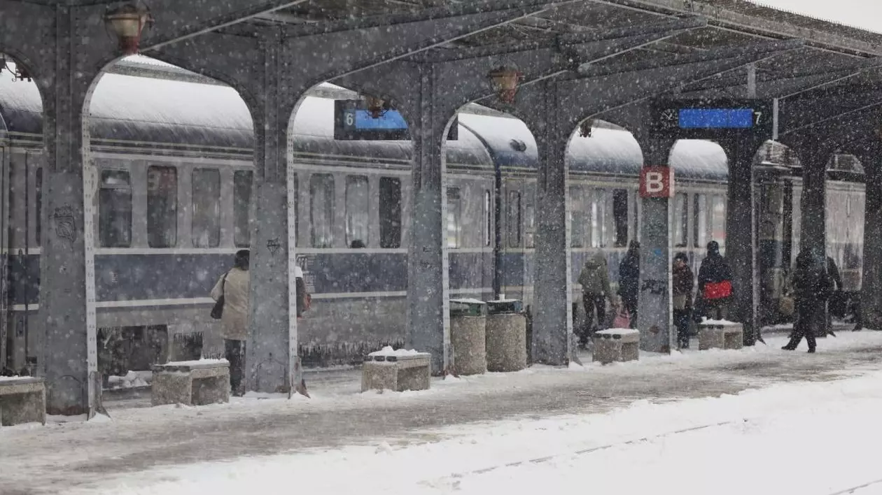 Imagine din Gara de Nord din București, cu un tren în gară și mai mulți oameni pe peron, într-o zi de iarnă, în care ninge