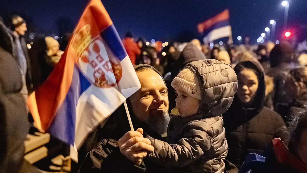 Un părinte își poartă în brațe copilul și flutură împreună un steag al Serbiei, la protestul anticorupție din Belgrad