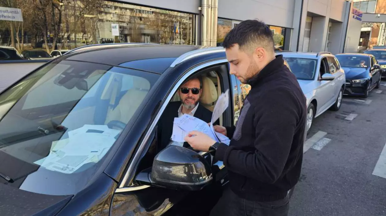 mai multe masini in linie pentru inspectia rar. un barbat tine in mana cateva documente pentru inspectie, in masina se afla un sofer