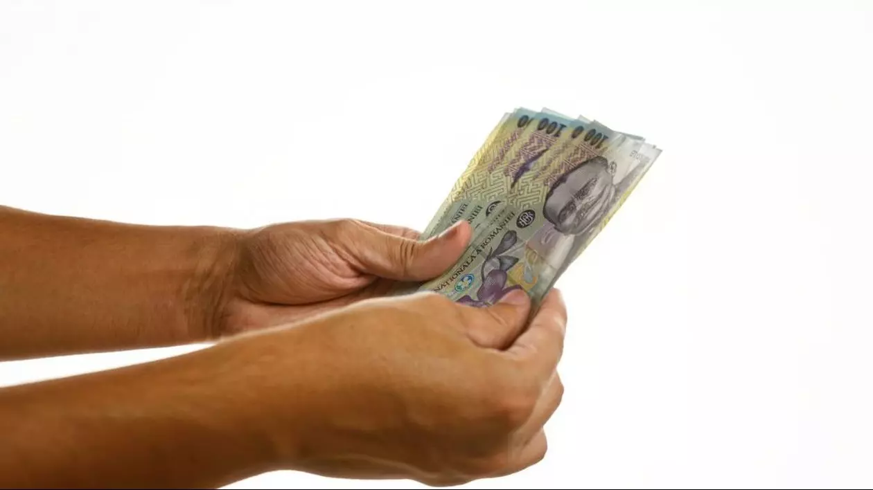 Mâinile unui bărbat care țin mai multe bancnote românești de 100 de lei, pe un fundal alb