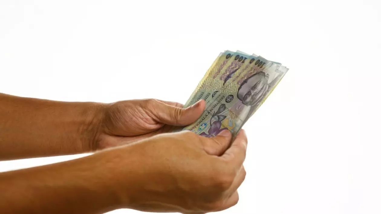 Mâinile unui bărbat care țin mai multe bancnote românești de 100 de lei, pe un fundal alb