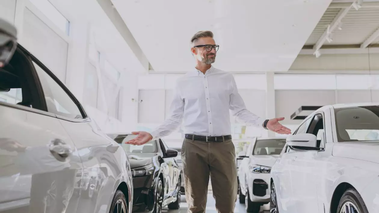 barbat imbracat cu o camasa alba aflat printre mai multe masini intr-un showroom auto