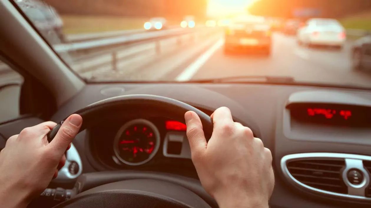 mainile unui sofer pe volanul masinii aflat in mers, pe o autostrada