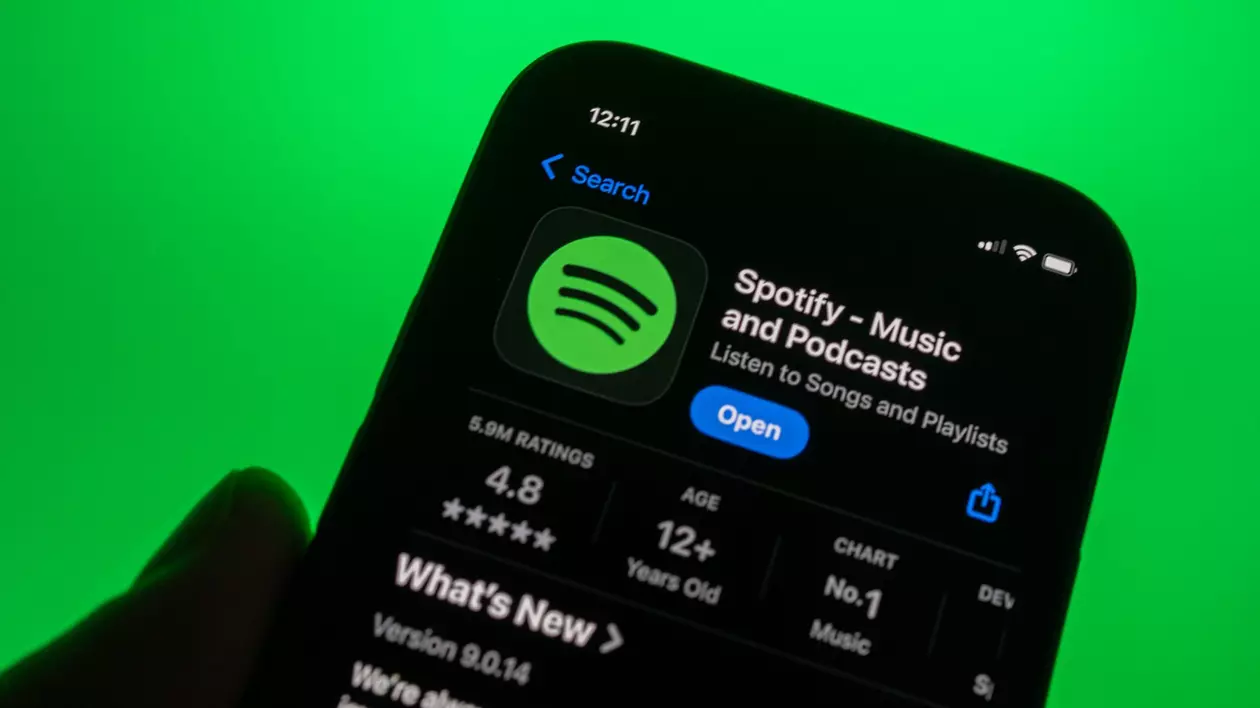 Pagina aplicației SPotify din AppStore, deschisă pe ecranul unui iPhone ținut în mână în fața unui fundal verde.
